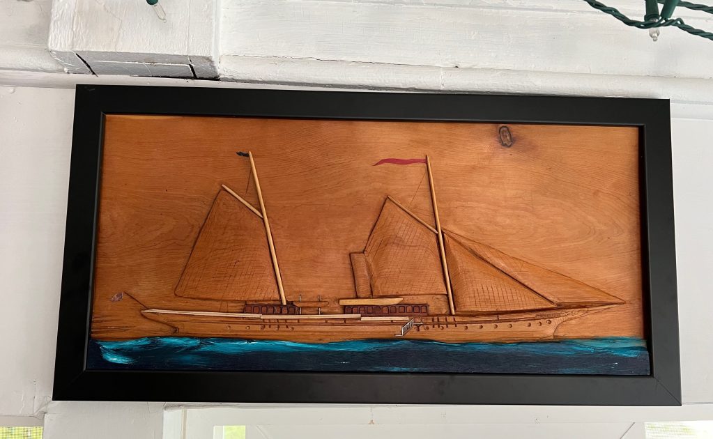 A carved wooden wall art depicting a sailboat in a nautical setting with a blue sea and a wooden background.