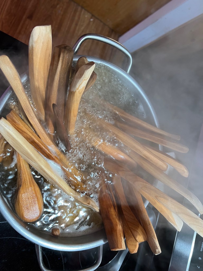 A pot of boiling water filled with multiple wooden cooking spoons, with steam rising from the surface.