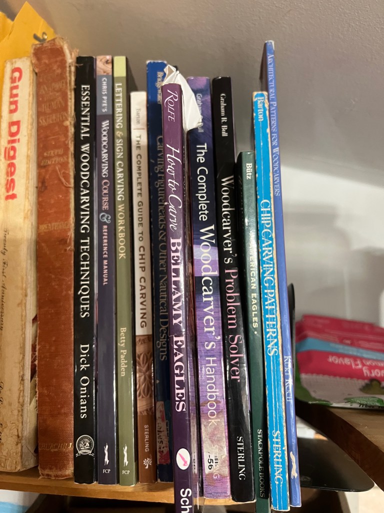 Close-up of a bookshelf filled with various woodcarving and woodworking books, including titles such as 'Essential Woodcarving Techniques' and 'The Complete Woodcarver's Handbook'.