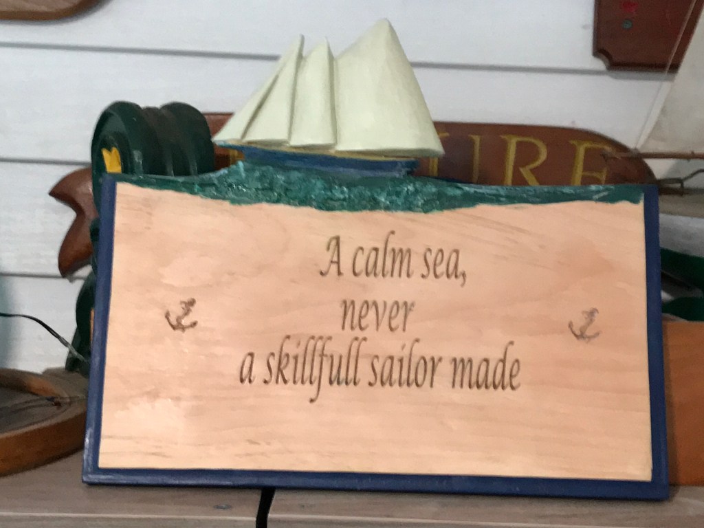 A wooden plaque with the inscription 'A calm sea, never a skillfull sailor made', featuring an anchor design.