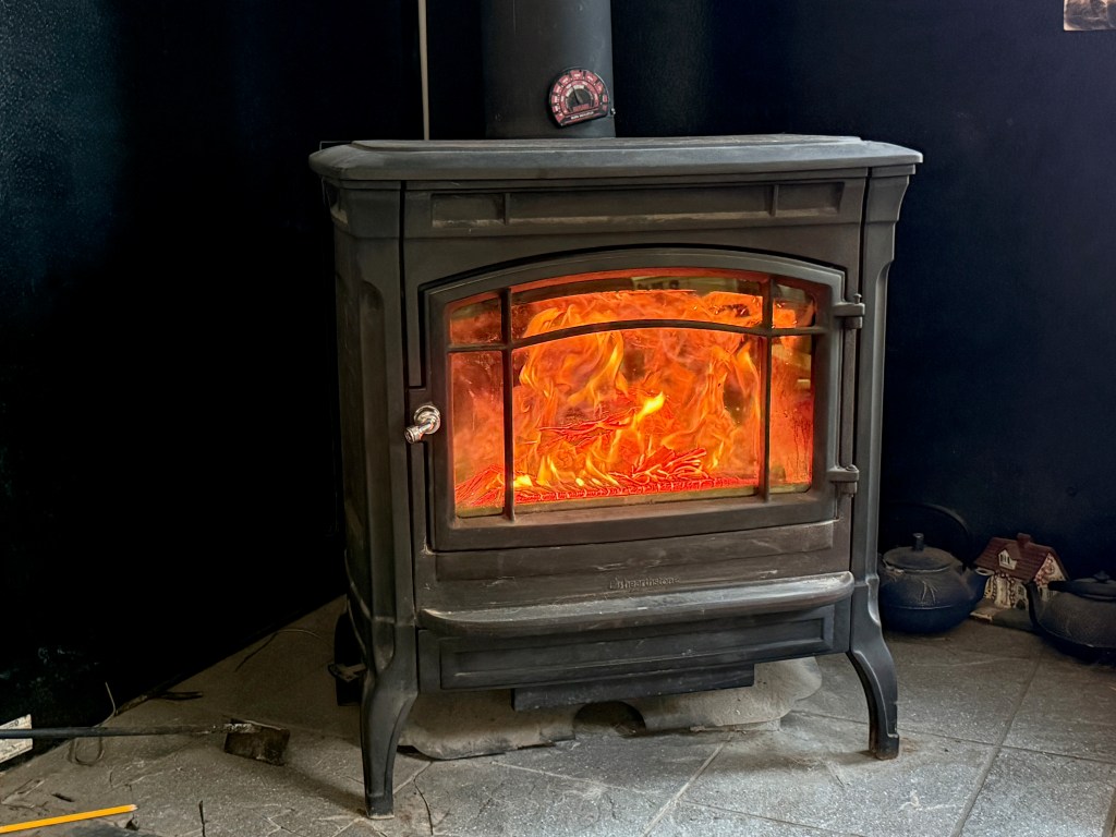 A black wood stove with a visible fire burning inside, surrounded by a dark room.