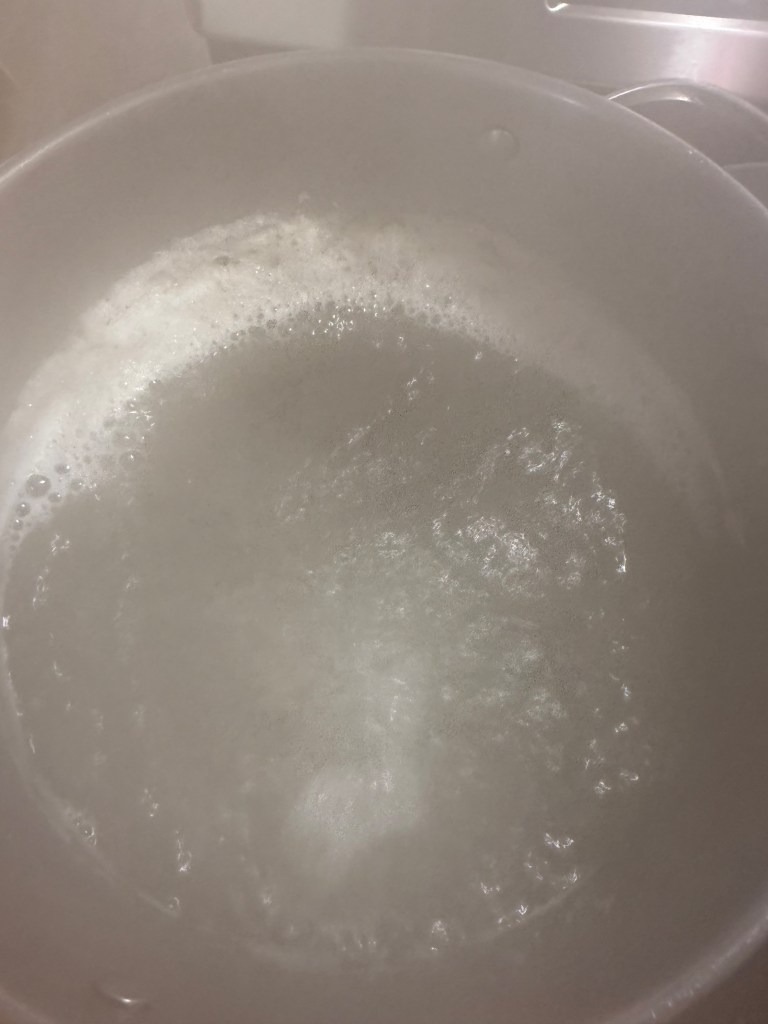 A close-up of simmering water in a cooking pot, with bubbles forming on the surface.