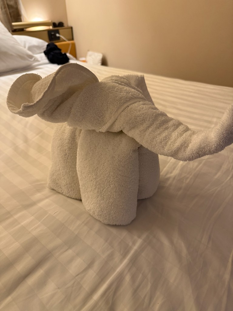 A towel sculpture shaped like an elephant, placed on a bed with a striped sheet.