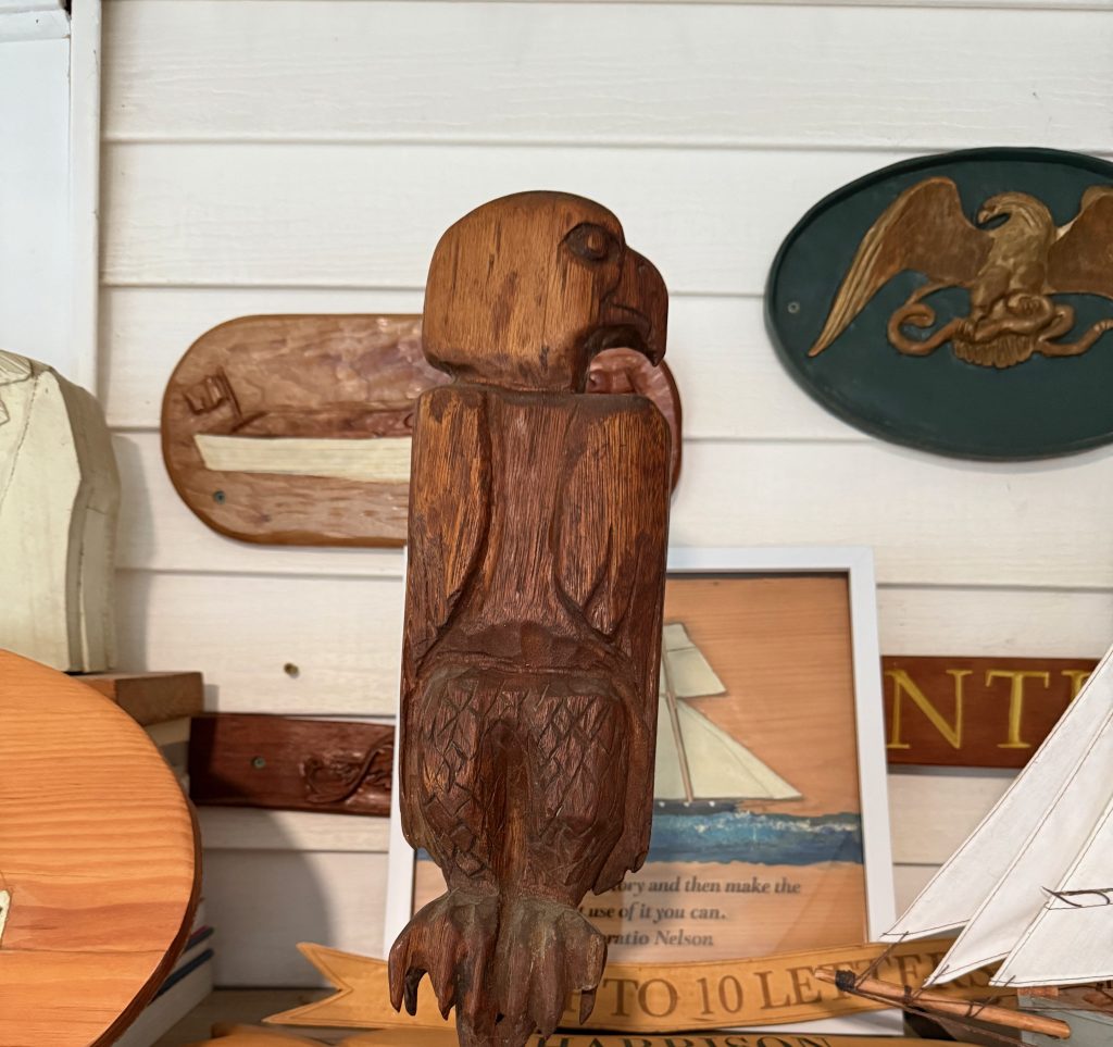 A wooden eagle sculpture displayed against a light-colored wall, surrounded by various decorative items.